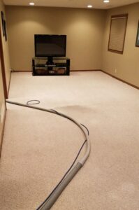 A residential room with light-colored carpet and a blue cleaning hose laid out, ready for service by Gemini Carpet Cleaning in Lincoln, NE