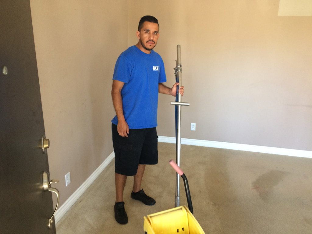 A carpet cleaning technician from Ace Janitorial Services, Inc. with a cleaning wand in a carpeted room in San Diego, CA.