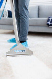 A Zerorez technician in shoe covers using a cleaning tool on a carpet, showing a clean strip, in Naperville, IL, by Zerorez ChicagoLand.