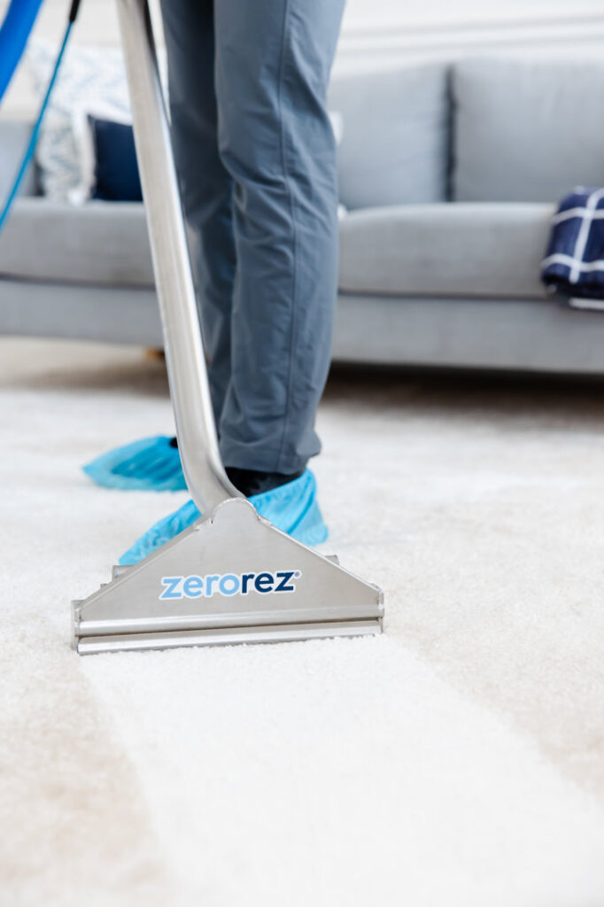 A Zerorez technician in shoe covers using a cleaning tool on a carpet, showing a clean strip, in Naperville, IL, by Zerorez ChicagoLand.