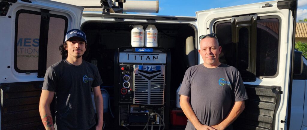 Two carpet cleaning technicians standing with their truck-mounted cleaning equipment at Healthy Homes Cleaning and Restoration LLC in Fort Lauderdale, FL.