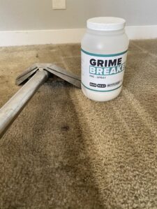 A carpet cleaning tool and 'Grime Breaker' pre-spray bottle on a carpet, used by Orozco's Janitorial Services LLC in Escondido, CA.