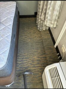 A carpet cleaning tool visible on a carpeted floor next to a bed, indicating a cleaning job by Carpet Cleaners Plus in Chicago, IL.