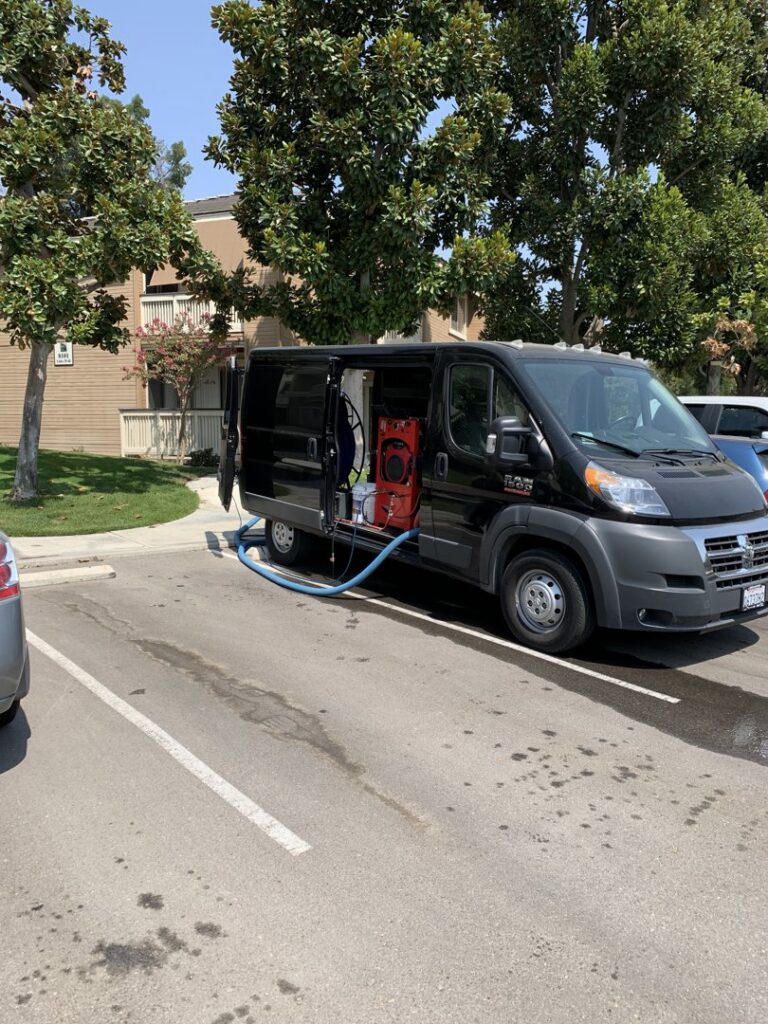 Koky's Carpet Cleaning truck-mounted system with hoses running into a building for a cleaning service in Bakersfield, CA