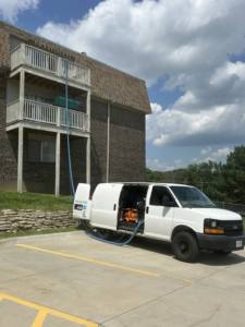 A Reliable Carpet Cleaning LLC van with a hose running to an apartment balcony for a job in Liverpool, NY.