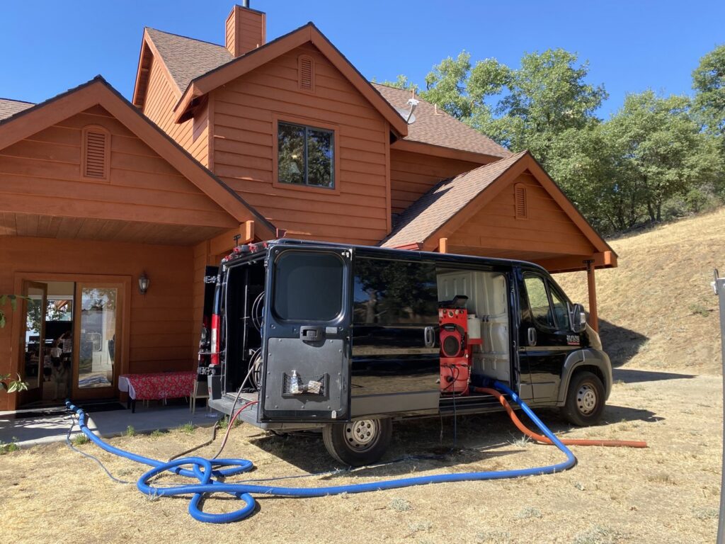 A Koky's Carpet Cleaning van with hoses extended into a residential home for a carpet cleaning job in Bakersfield, CA