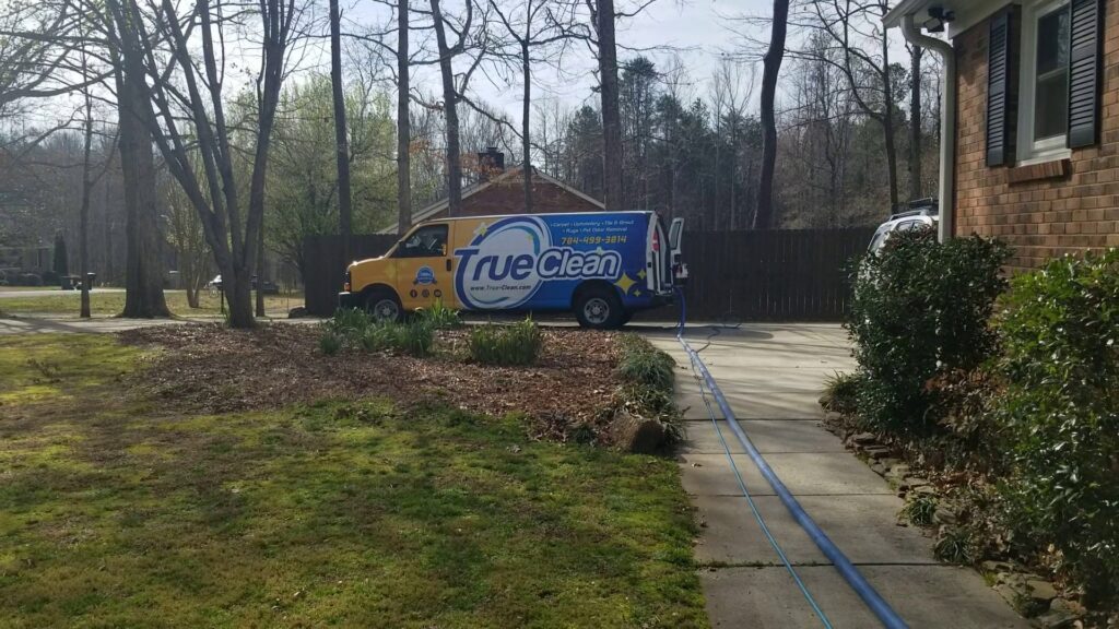 A True Organic Carpet Cleaning van with hoses running to a house, ready for service in Charlotte, NC.