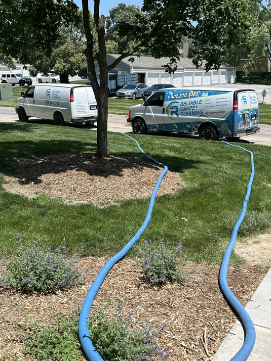 Two Reliable Carpet Cleaning LLC vans with hoses extended, ready for a carpet cleaning job in Liverpool, NY.