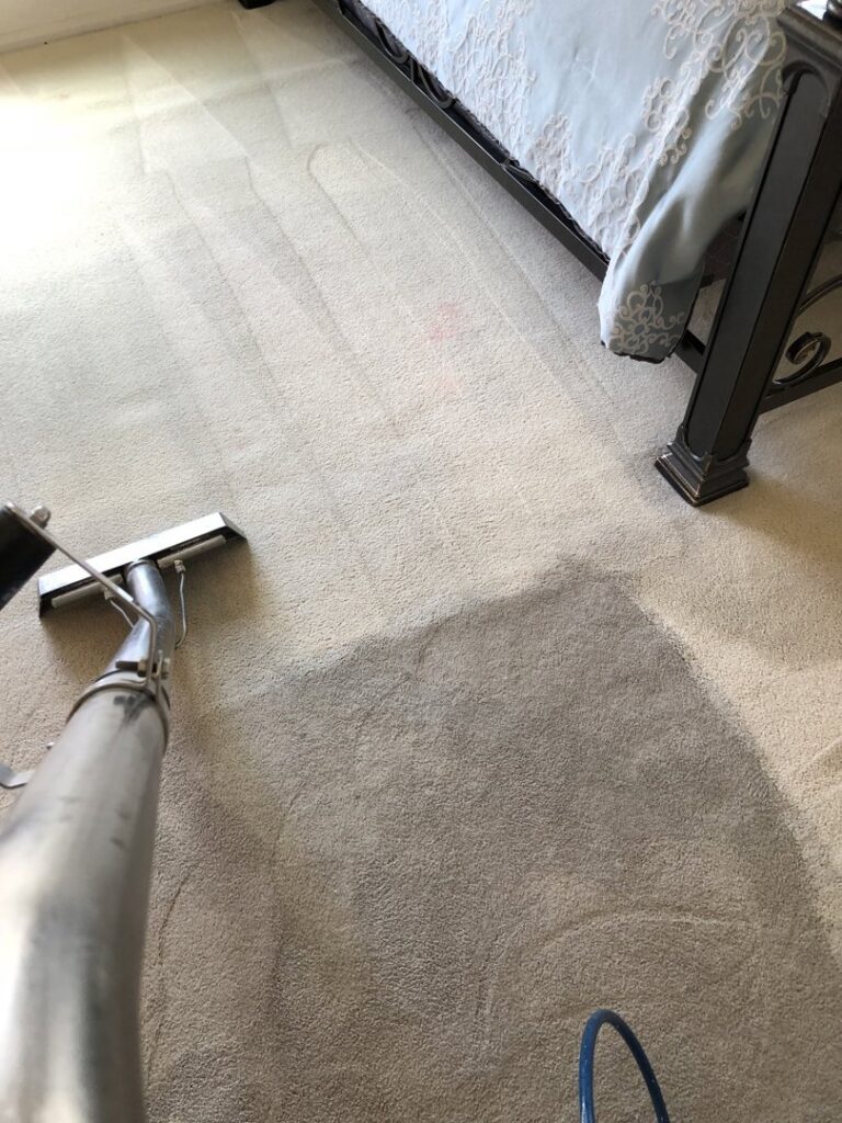 A carpet cleaning wand in use on a bedroom carpet, demonstrating the cleaning process by Fletcher's Carpet Cleaning & Stretching in Knoxville, TN.