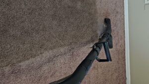 A carpet cleaning wand in action, showing a clean path on brown carpet by Andy's Cleaning Company LLC in Topeka, KS.