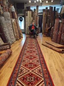 A carpet contractor sitting in the Borokhim's Oriental Rugs showroom, featuring a long, patterned oriental rug runner on display in Madison, WI.
