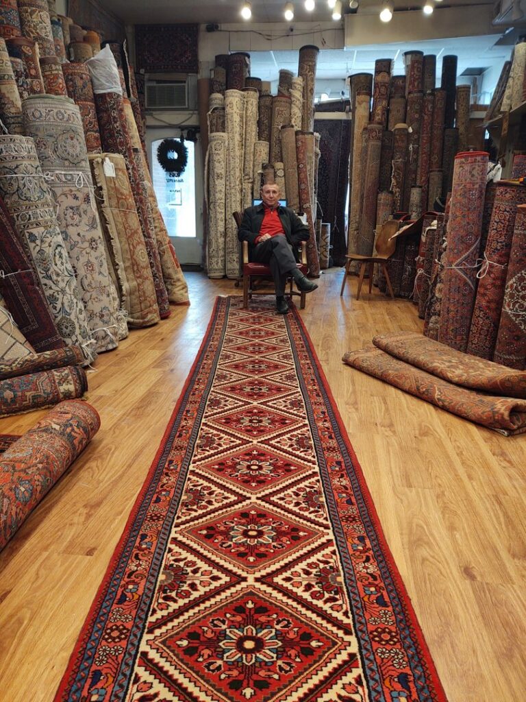 A carpet contractor sitting in the Borokhim's Oriental Rugs showroom, featuring a long, patterned oriental rug runner on display in Madison, WI.