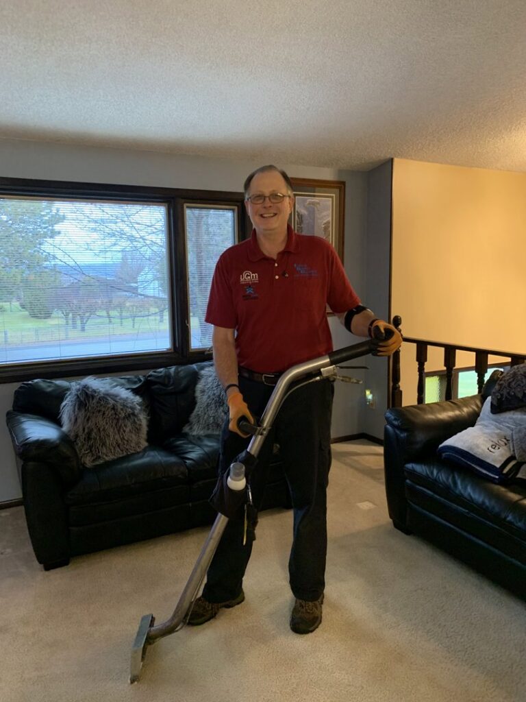 A professional carpet contractor from Lund's Carpet Cleaning holding cleaning equipment in a client's living room in Spokane, WA.
