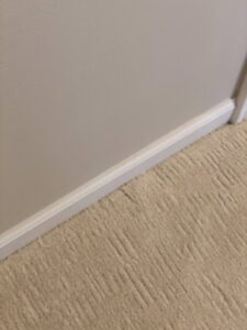 Detailed view of light-colored carpet edge installation against a white baseboard by Floor Gallery in Pearland, TX