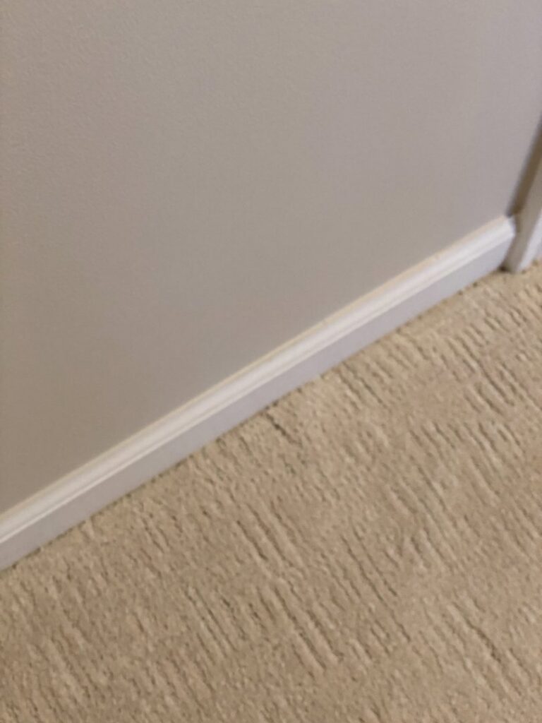Detailed view of light-colored carpet edge installation against a white baseboard by Floor Gallery in Pearland, TX