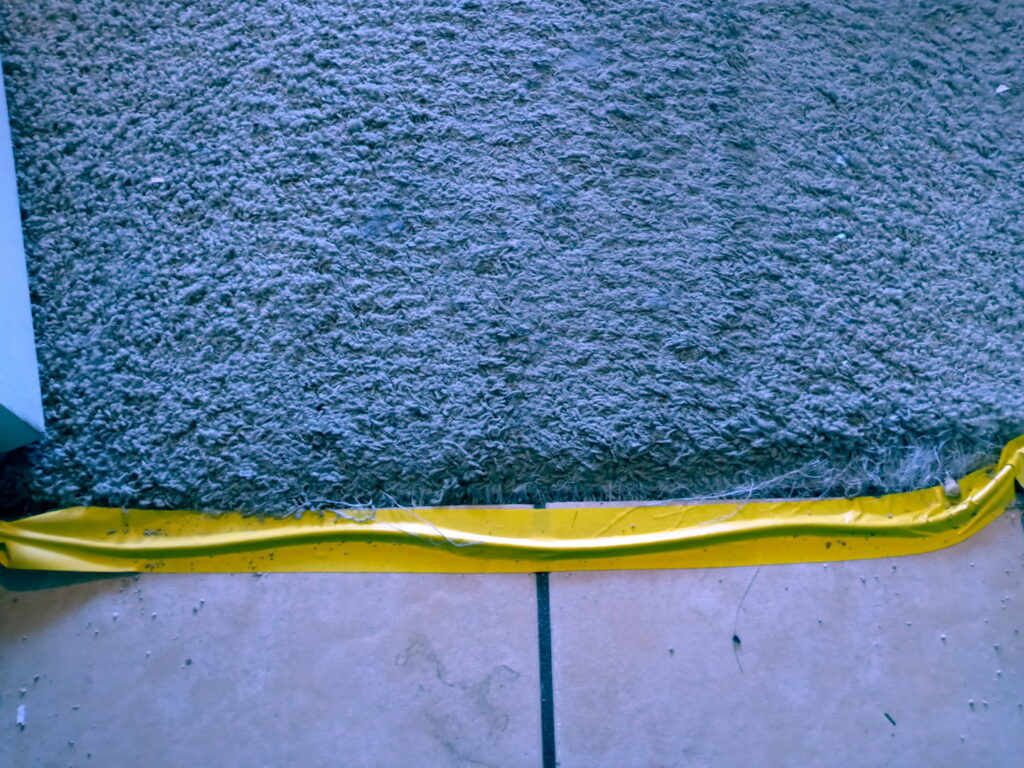 A carpet edge protected with yellow tape during work by Tucson Carpet Repair & Cleaning in Tucson, AZ.
