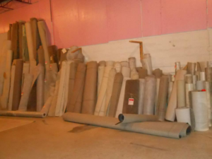 A warehouse storage area filled with various rolls of carpet and flooring materials at Frosty's Carpet Center, Inc. in Grand Forks, ND.