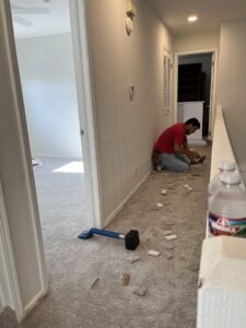 A carpet installer working on a new carpet installation in a residential hallway, demonstrating the services of B A Carpet and Flooring in Broken Arrow, OK.
