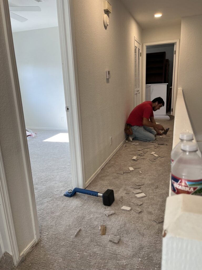 A carpet installer working on a new carpet installation in a residential hallway, demonstrating the services of B A Carpet and Flooring in Broken Arrow, OK.