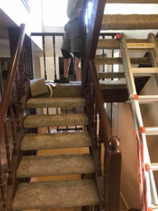 Carpet installation or removal in progress on a staircase, with a worker and ladder, by Brett's Pro Carpet Repair in Fort Collins, CO.