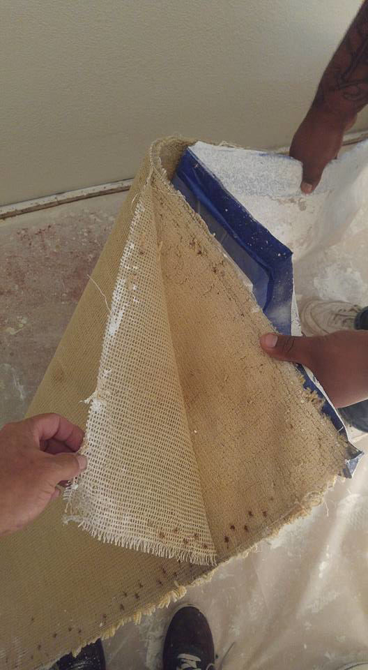 Hands lifting carpet to reveal the backing and subfloor during a carpet installation or removal job by Renaissance Carpet Cleaning in Henderson, NV.