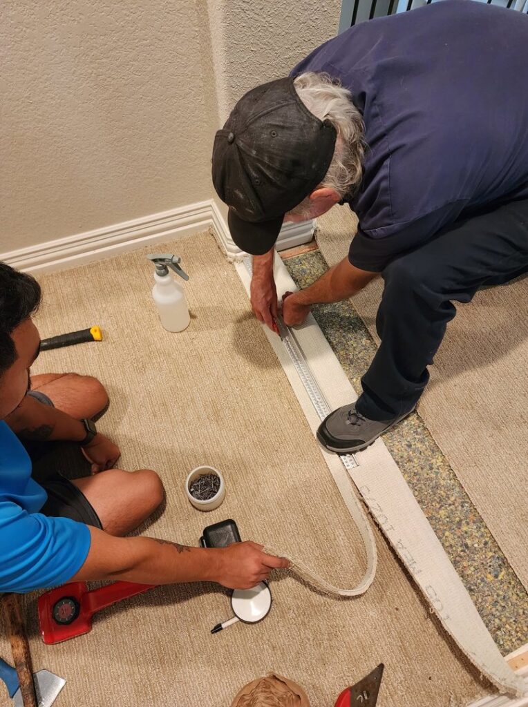 Two technicians performing carpet installation or repair work, measuring and preparing the carpet, for Carpet Care Express in Garland, TX