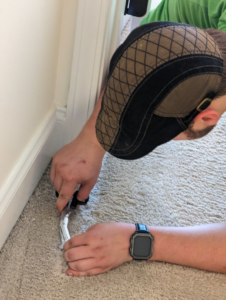 A carpet contractor performing installation or repair work on carpet near a baseboard for Top Floor Carpet Cleaning in Lenoir City, TN.