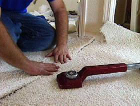 A carpet installer using a knee kicker tool to stretch and install new carpet at Delgado Carpet Services in San Jose, CA