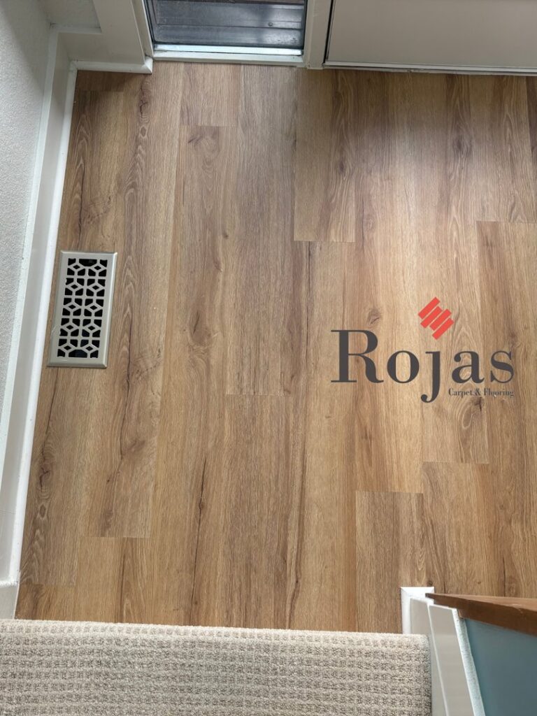 A view from above showing a transition from wood-look laminate flooring to new carpet at the base of a staircase by Rojas Carpet and Flooring in Denver, CO.