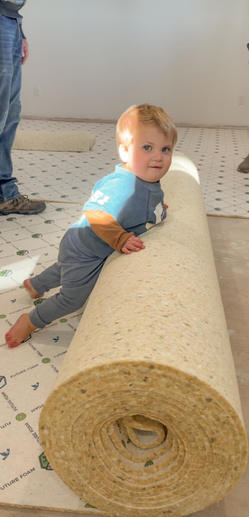 Carpet padding being installed on a floor by Carpet Mart Inc in Janesville, WI, showing a roll and laid sections.