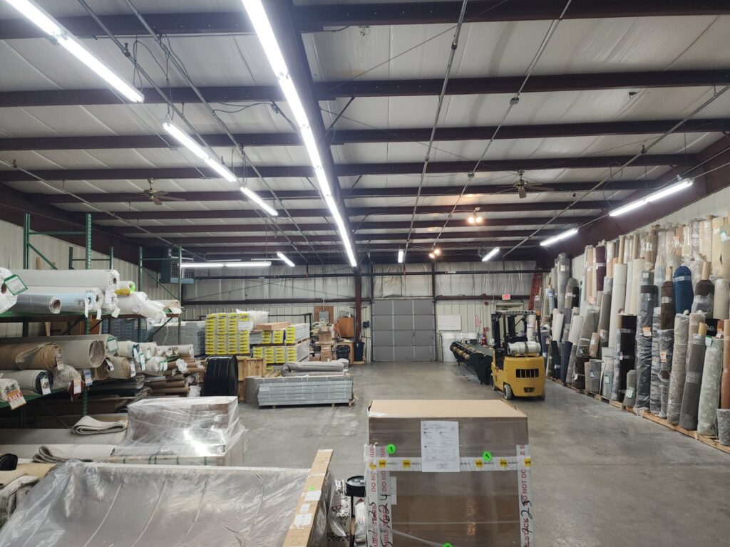 A vast warehouse with numerous rolls of carpet and other flooring materials at CarpetsPlus Colortile in Swansea, MA
