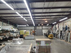 A vast warehouse with numerous rolls of carpet and other flooring materials at CarpetsPlus Colortile in Swansea, MA