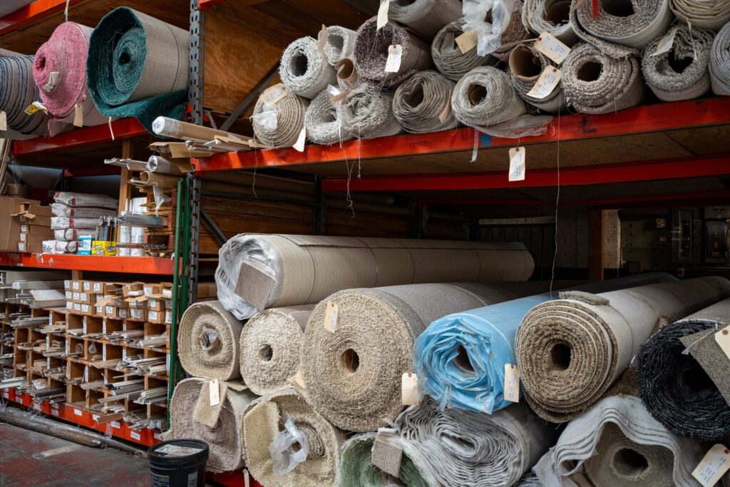 Close-up view of various rolls of carpet and flooring materials stored on shelves at Mill Sales Co. in Los Angeles, CA
