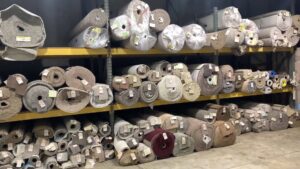 Rows of various carpet rolls neatly stacked on warehouse shelves, showcasing inventory at Gator Carpet and Tile in Jacksonville, FL.