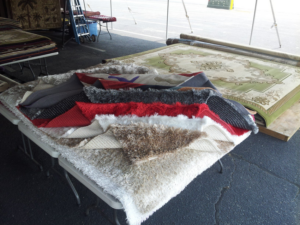 Various carpet rolls and rug samples displayed on tables by Sunshine Rugs and Art in Londonderry, NH.
