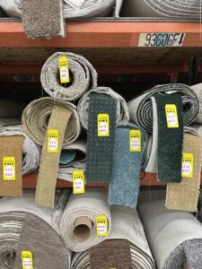 Rolls of various carpets displayed on shelves with 'SALE' tags in the warehouse of Sy's Discount Carpets in Los Angeles, CA