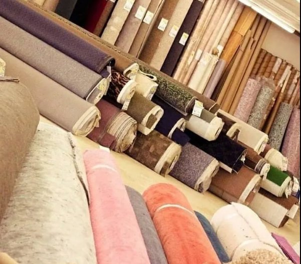 Numerous rolls of carpet in various colors and textures stacked in the showroom at AFAB Carpets in Tampa, FL.