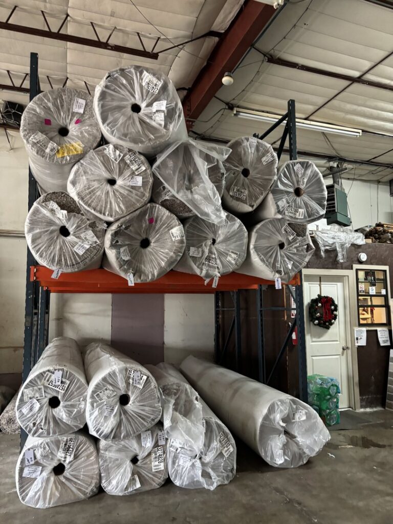 Rolls of carpet stored on shelves in a warehouse, ready for installation by Castro's Carpet in Houston, TX.