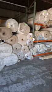 Large rolls of various carpets stacked in a warehouse, representing the extensive inventory available at Floors By Tomorrow in Aurora, CO