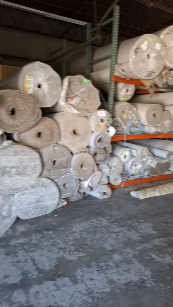 Large rolls of various carpets stacked in a warehouse, representing the extensive inventory available at Floors By Tomorrow in Aurora, CO