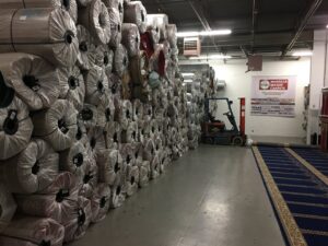 Warehouse filled with numerous rolled carpets and a forklift, managed by Musalla Masjid Carpets in Glendale Heights, IL.