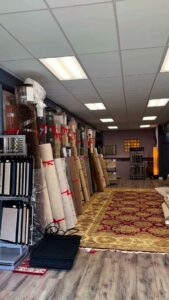 Rolls of carpet and a large area rug displayed in the showroom of Morency Flooring in New Bedford, MA.