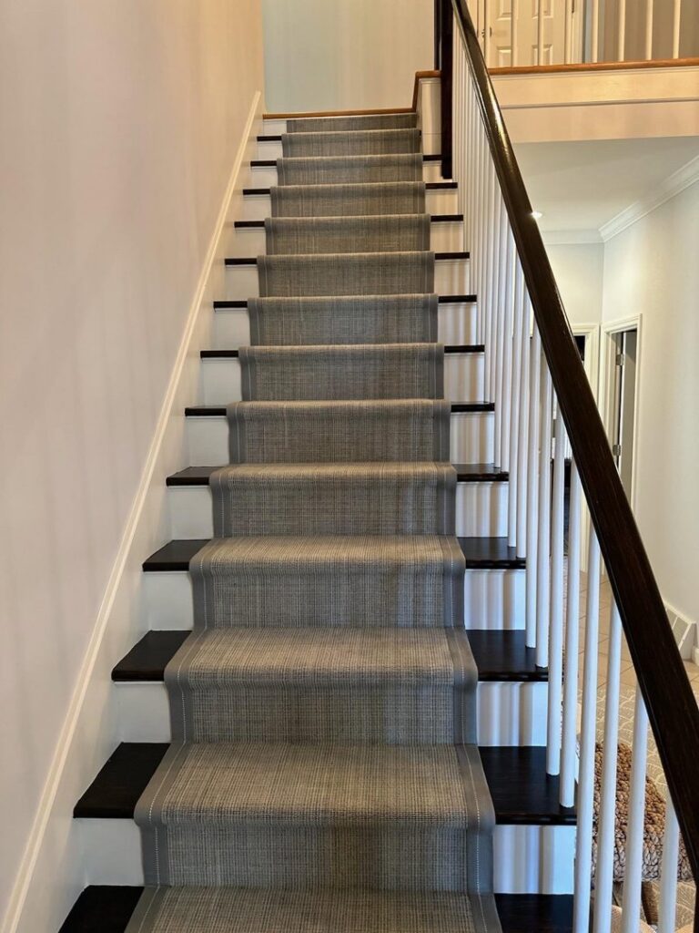 A newly installed gray carpet runner on a dark wood staircase by Floor Coverings International South Rhode Island in Westerly, RI.