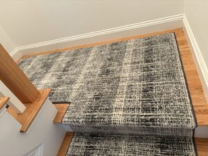 A professionally installed carpet runner on a wooden staircase by Paul White Company in Portland, ME.