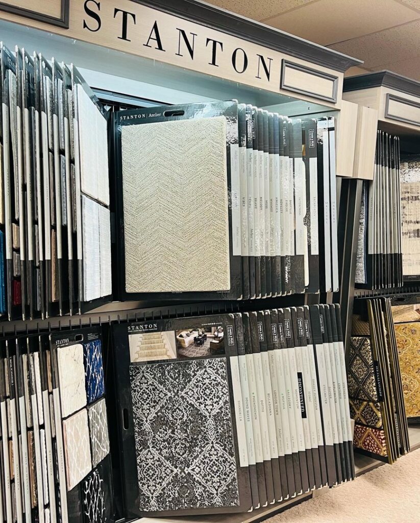 Rows of carpet samples on display racks in the showroom of All Surfaces Wholesale in Houston, TX.