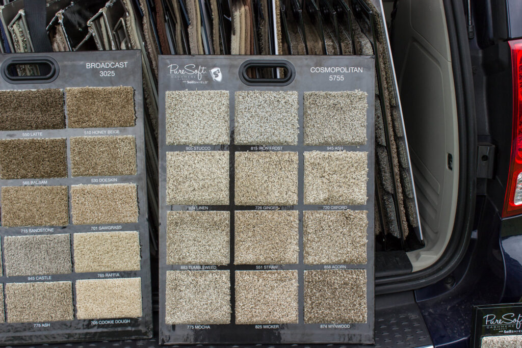 Carpet samples displayed on two boards in a vehicle, showing options from Home Based Carpet & Flooring in Cincinnati, OH.