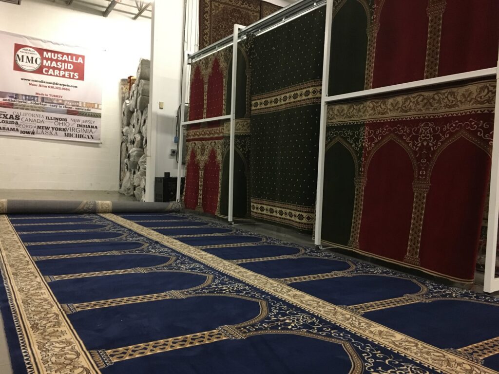 Carpet rolls displayed in a showroom with a partially unrolled blue carpet by Musalla Masjid Carpets in Glendale Heights, IL.