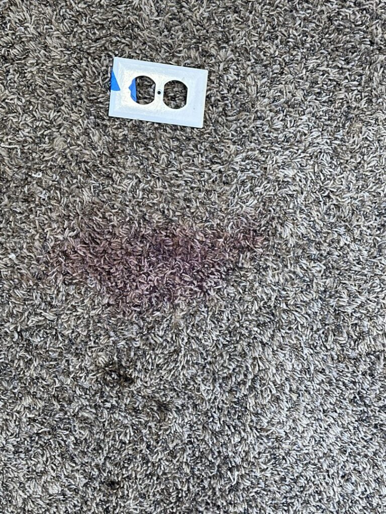 A visible stain on a carpet next to an electrical outlet, indicating a need for professional cleaning by Mountain View Carpet Care in Vancouver, WA