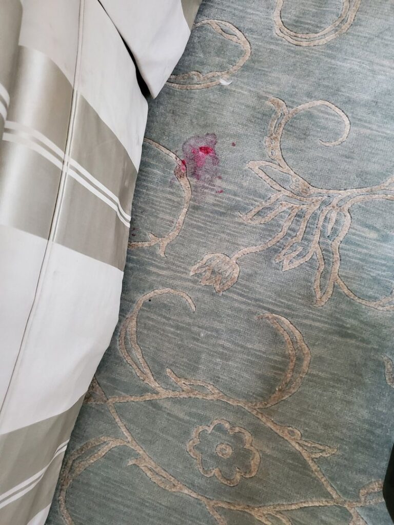 A red stain on a patterned area rug, indicating professional carpet stain removal by Genie Clean Services LLC in Dallas, TX.
