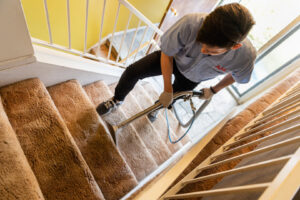 A technician performing carpet stair cleaning with a professional wand tool for AJS Carpet Cleaning, Inc. in Orem, UT.